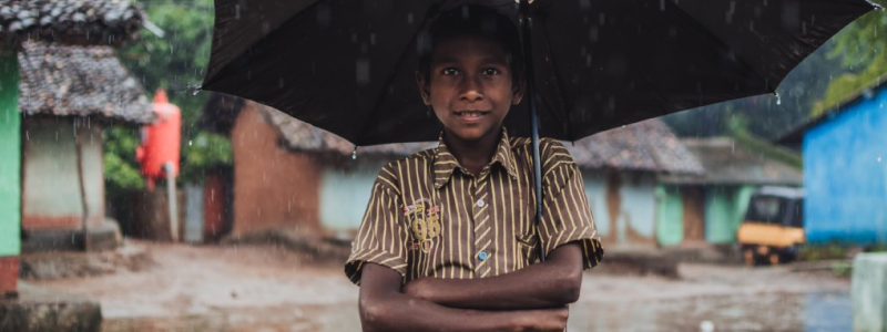 A photo of a smiling young boy holding an umbrella in the rain